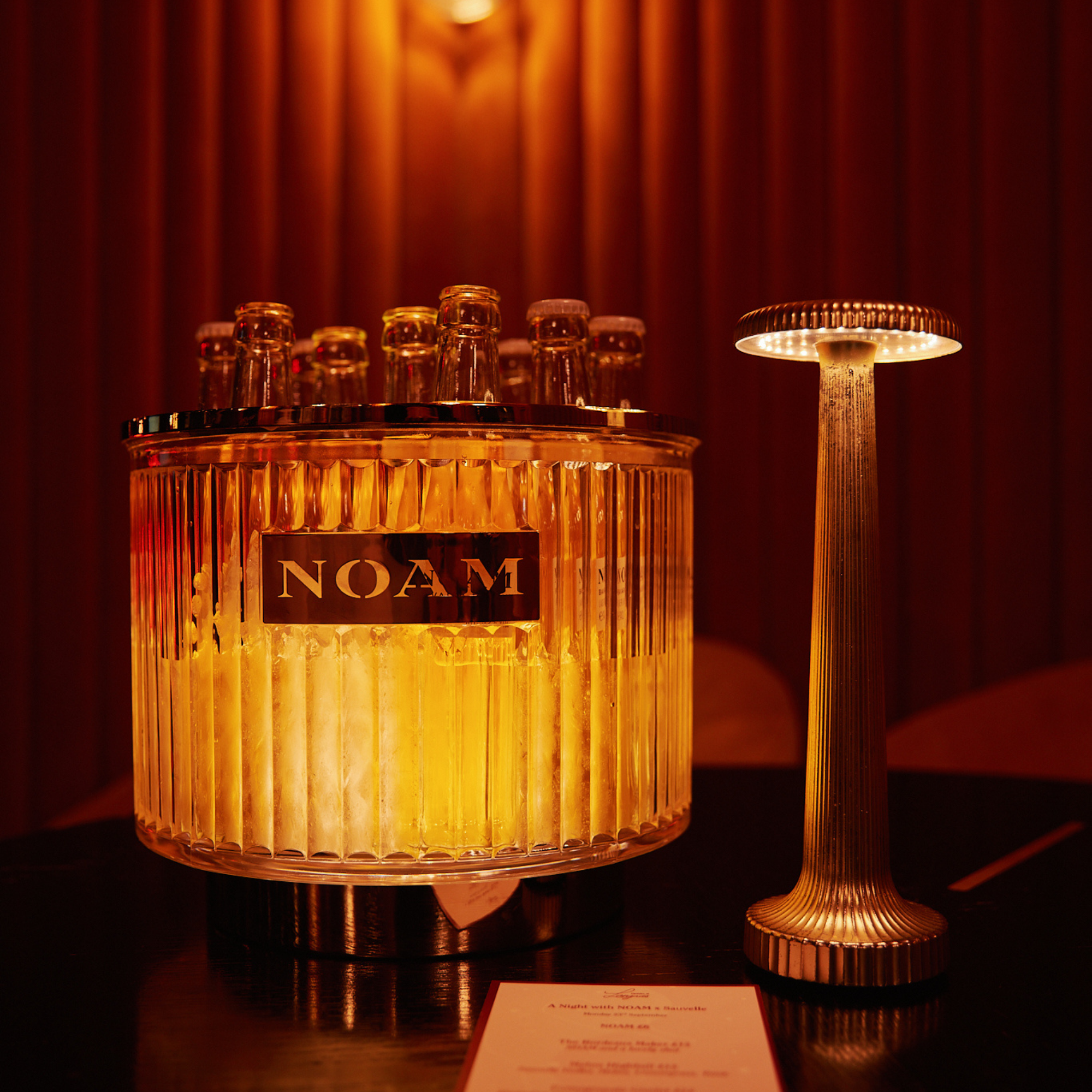Decorative bottle holder with 'NOAM' branding on a dark background