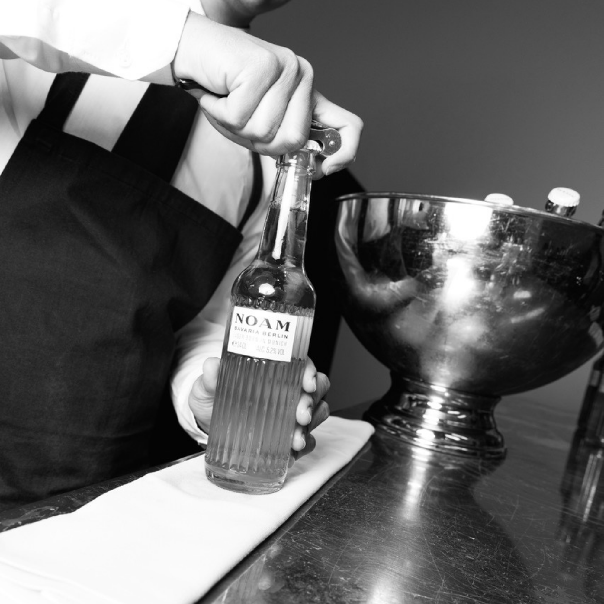 Person holding a bottle labeled 'NOAM' with a metallic bowl in the background
