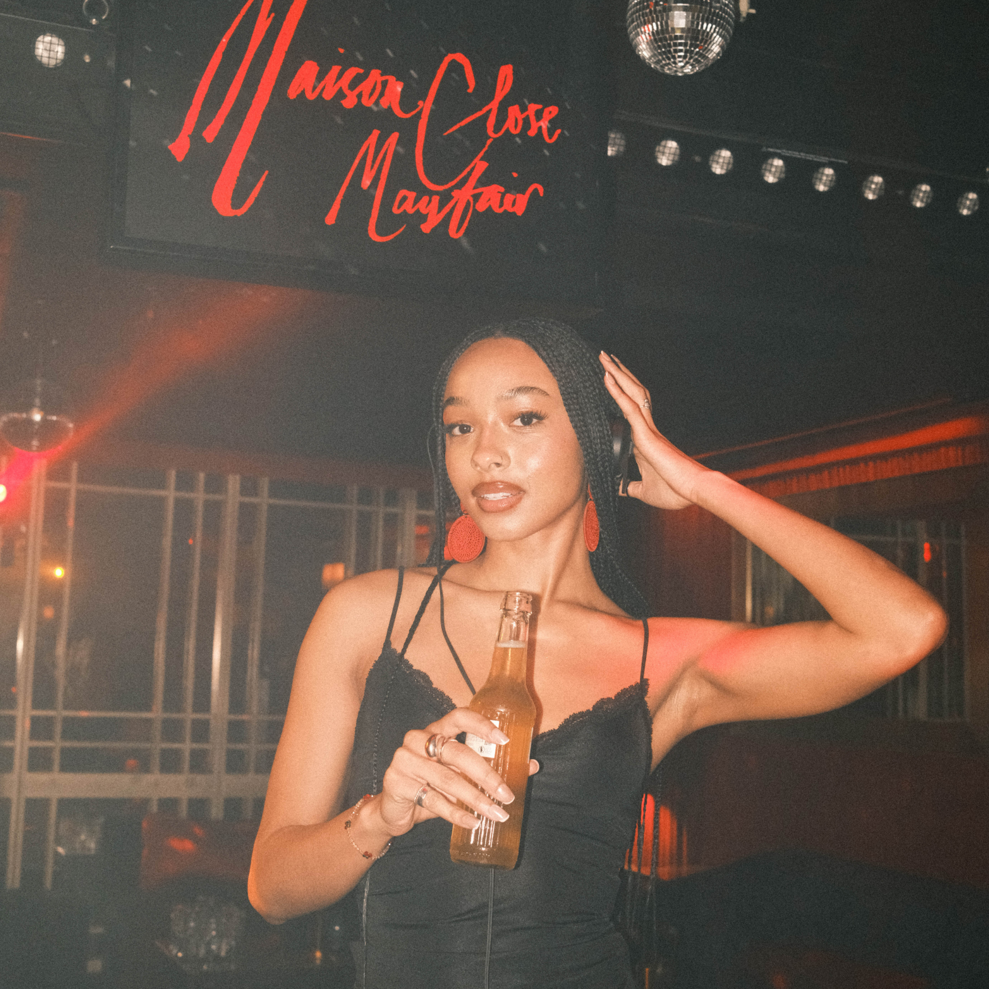 Woman holding a drink in a nightclub setting with 'Maison Close Mayfair' sign.
