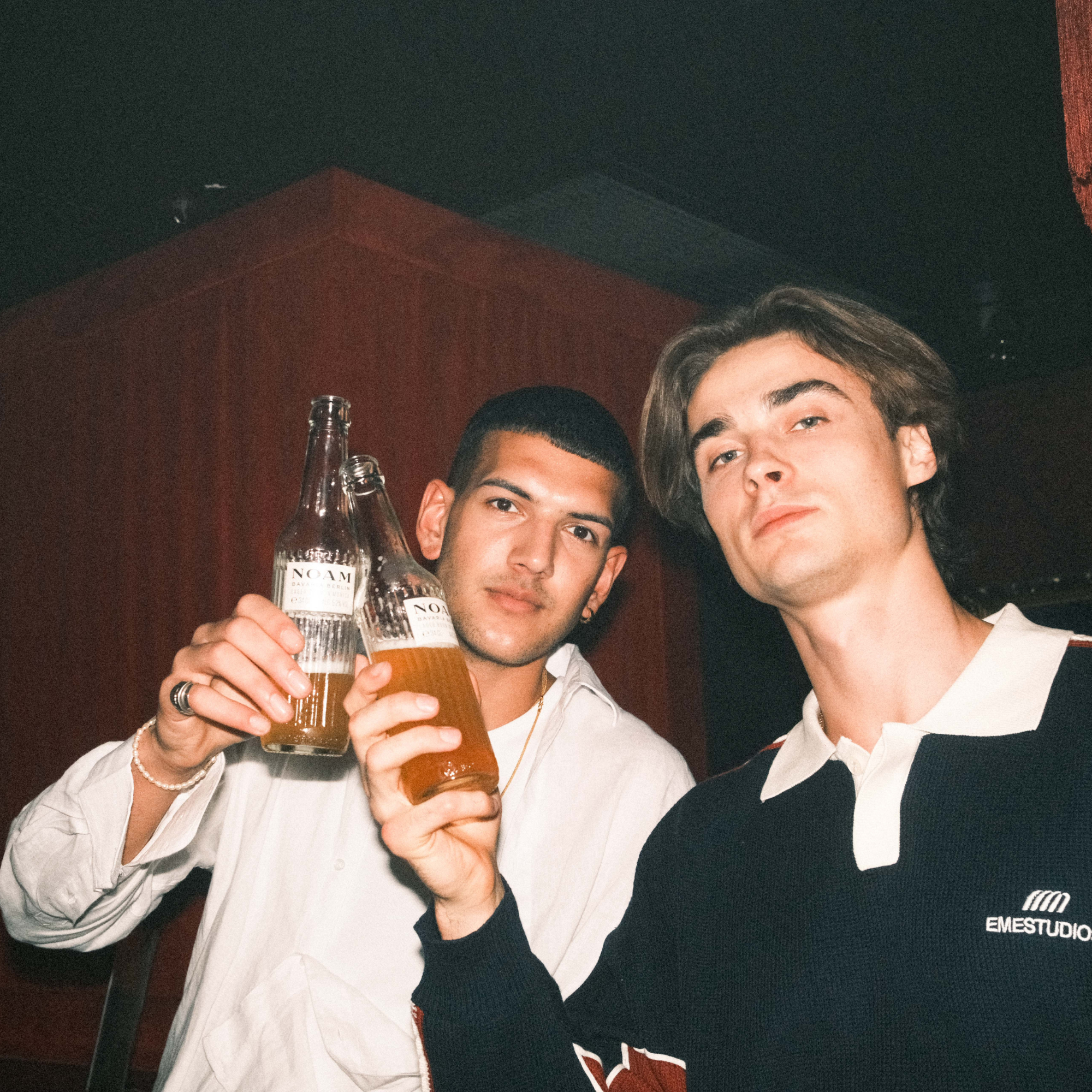 Two men holding drinks in a casual setting with a dark background