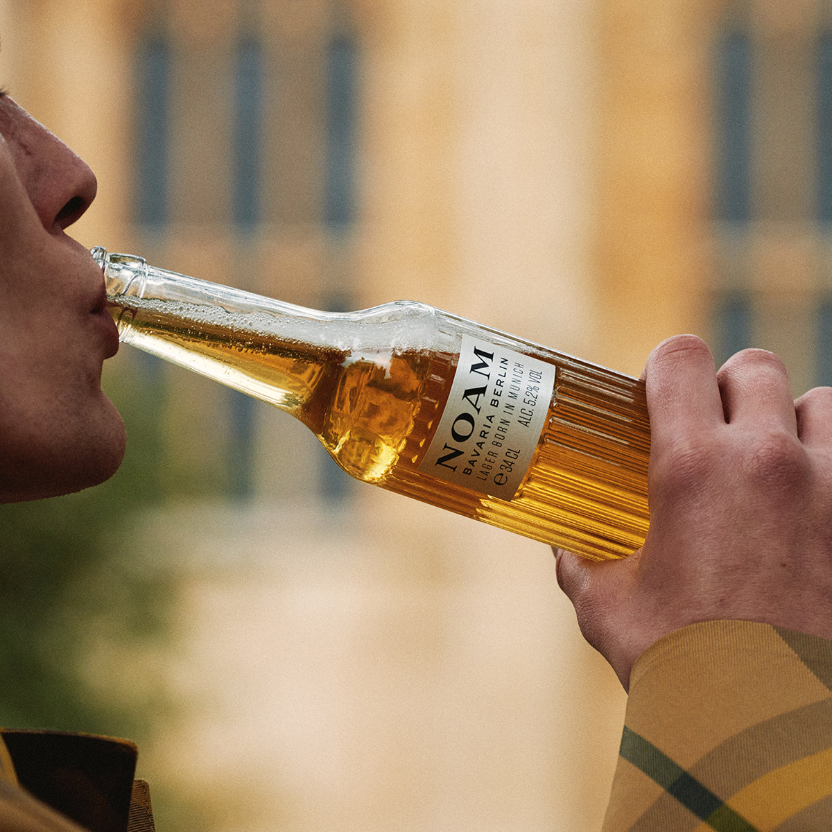 Person drinking from a bottle of NOAM beer with a blurred background
