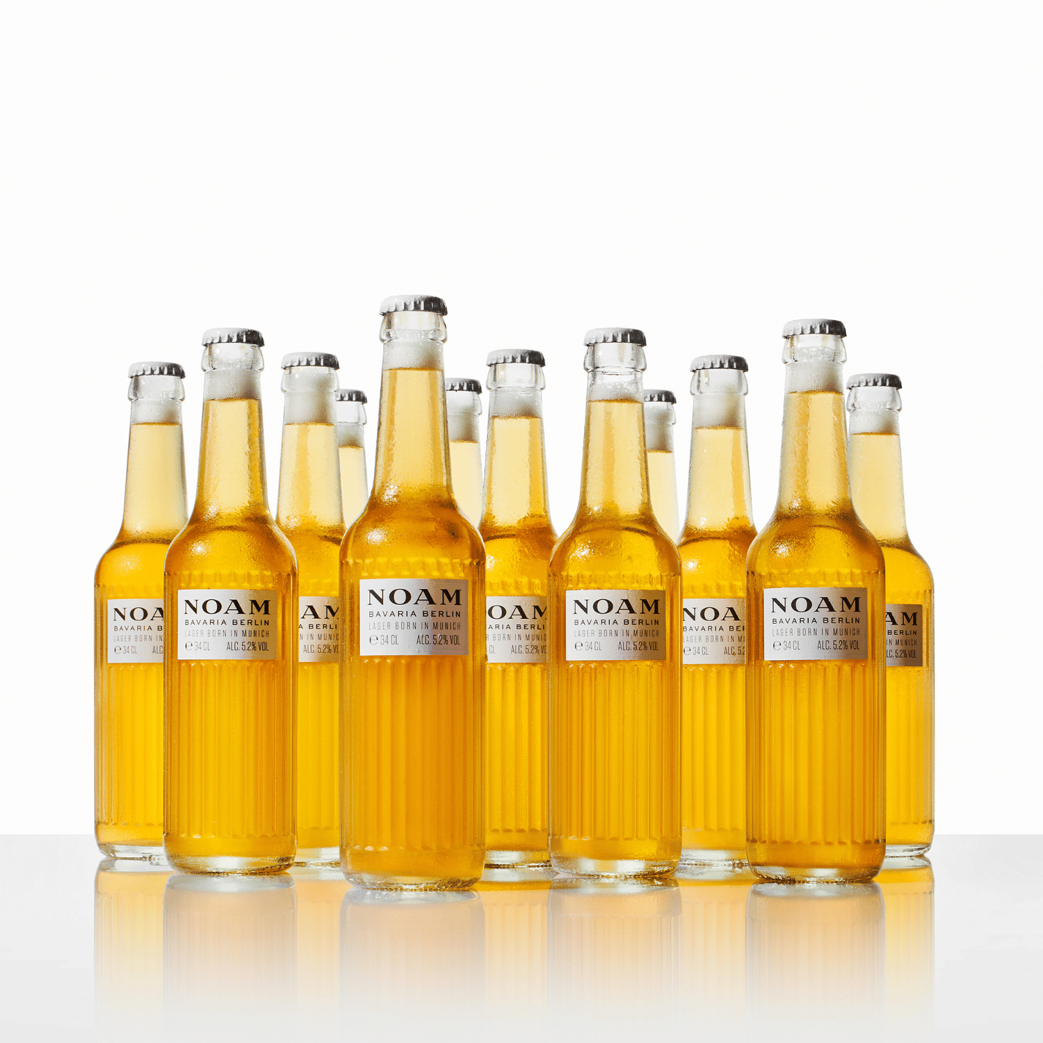 Multiple clear glass bottles filled with amber-colored beer, labeled NOAM, arranged in a row.