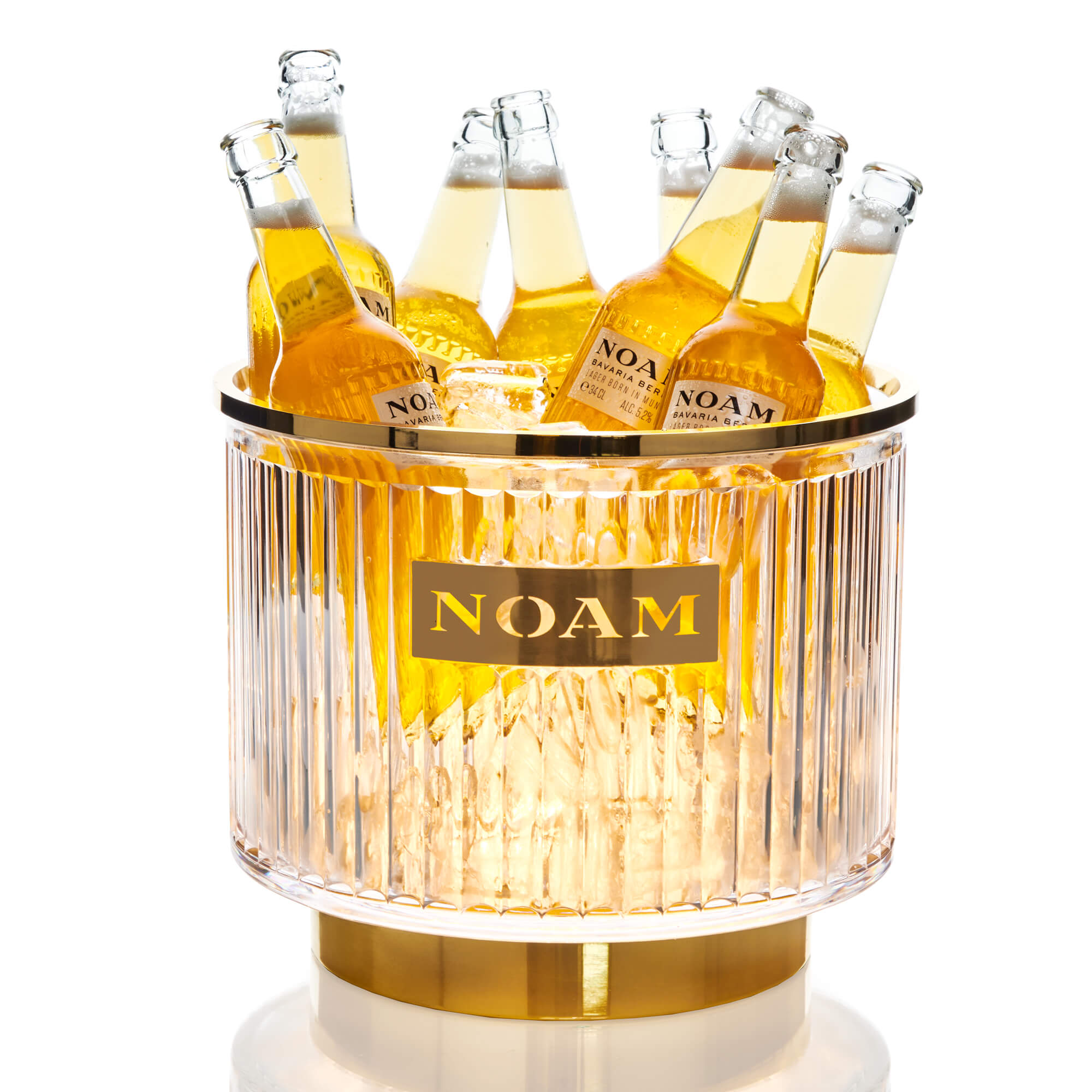 A clear glass cooler with a gold base, labeled 'NOAM', filled with bottles, with an LED light illuminating the contents.