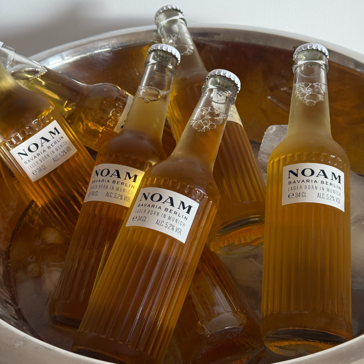 Bottles of NOAM beer in a metal ice bucket with ice cubes.