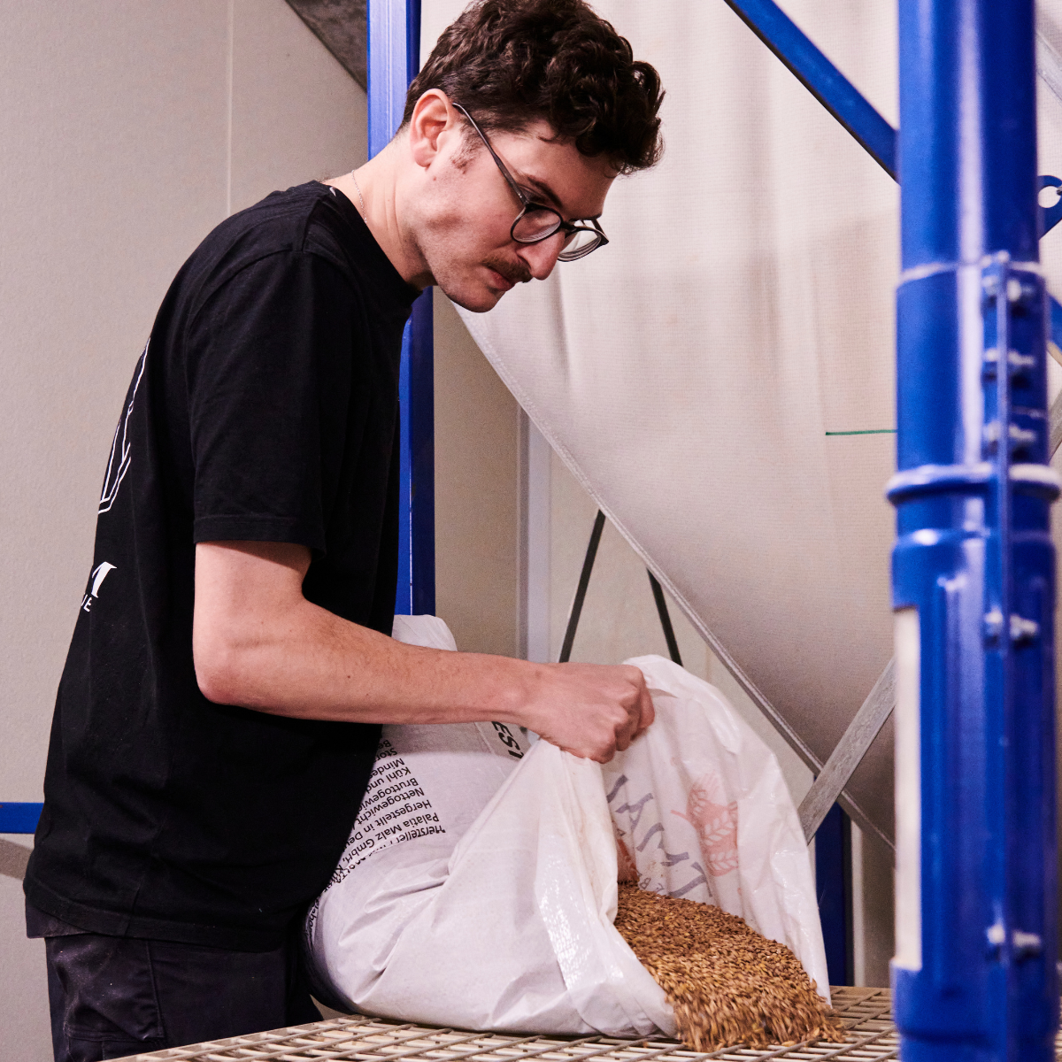 Person packaging items into a white bag in an indoor setting with blue metal structures.